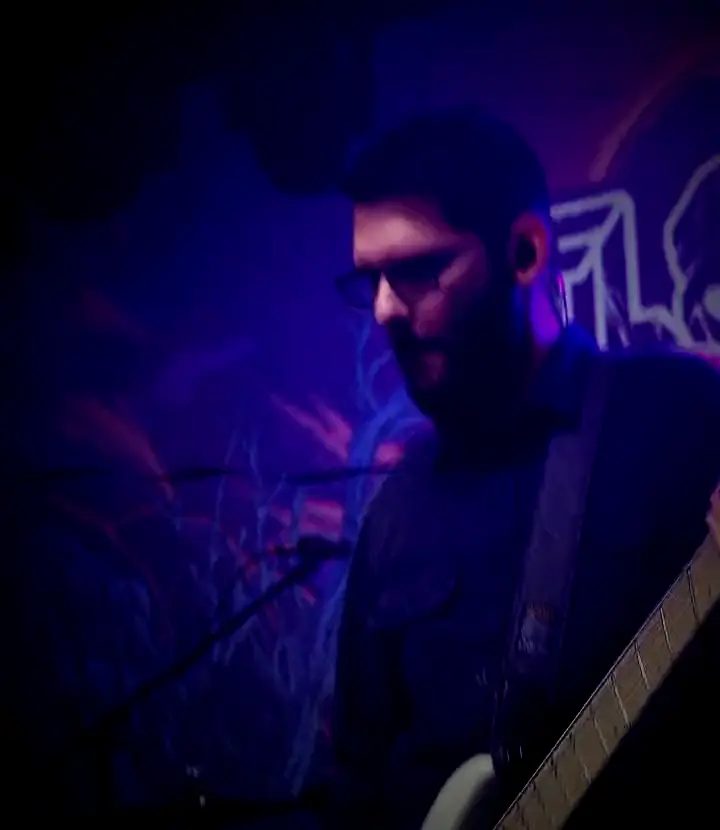 Lengyel Dávid basszusgitározik a FLOUT-logó előtt, narancs és lila fényben